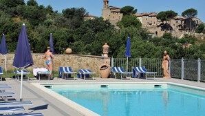 Une piscine avec des chaises longues et des parasols, une statue et un mur de pierre, avec un bâtiment en arrière-plan.