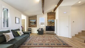 A living room with a green sofa, a patterned rug, wooden flooring, a TV, and a staircase.