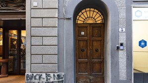 A building entrance with a wooden double door, a brick wall, and a small step leading up to the door.