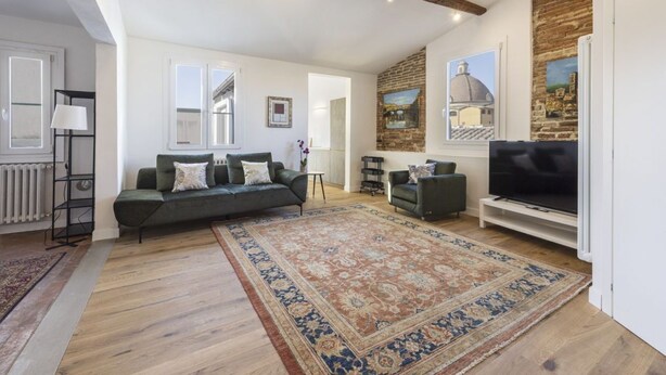 A spacious living area with a large sofa, a television, and a patterned rug.