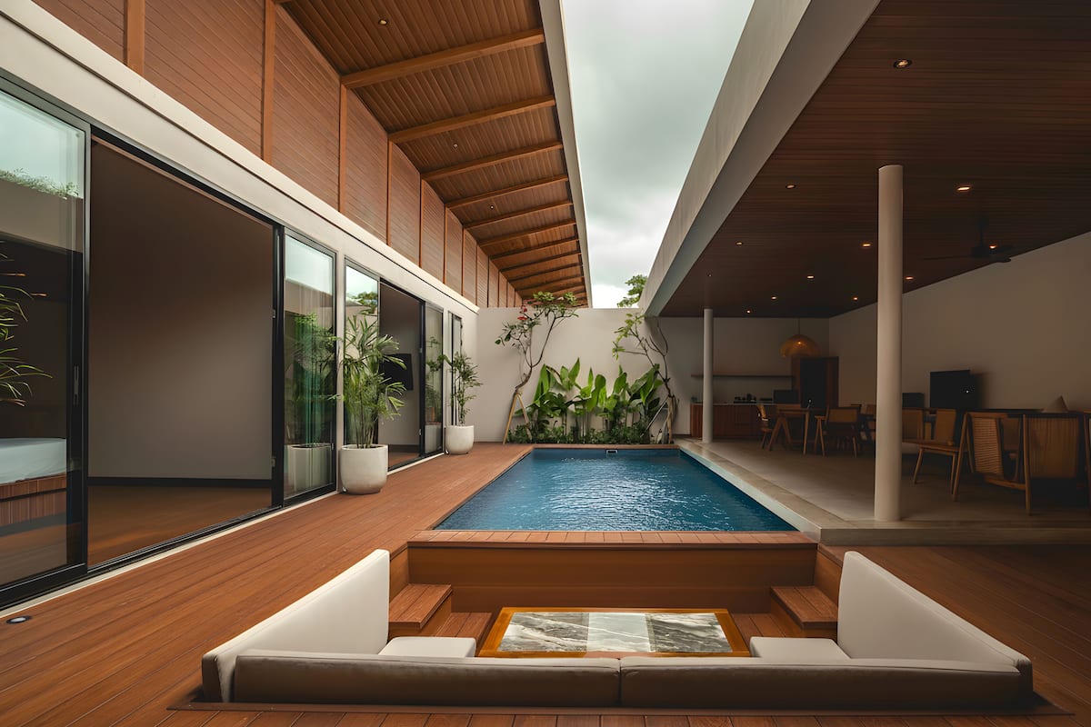 Uma área interna de piscina moderna com piso de madeira, um espaço de estar com almofadas e plantas em vasos.