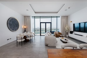 A modern living room with a dining area, large windows, and a flat-screen TV.
