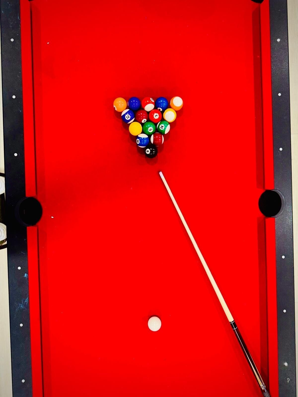 Una mesa de billar roja con disposición triangular de bolas de billar y una vara.