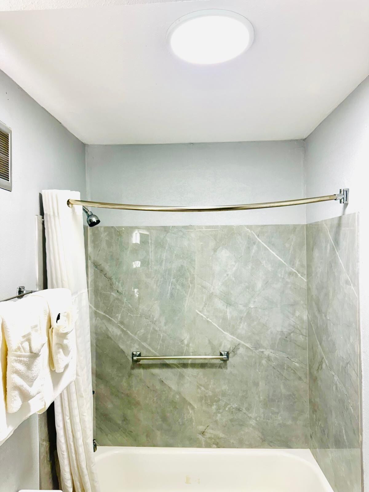 A modern bathroom with a glass shower enclosure, a bathtub, and a marble wall.