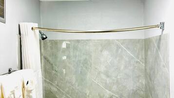 A modern bathroom with a glass shower enclosure, a bathtub, and a marble wall.