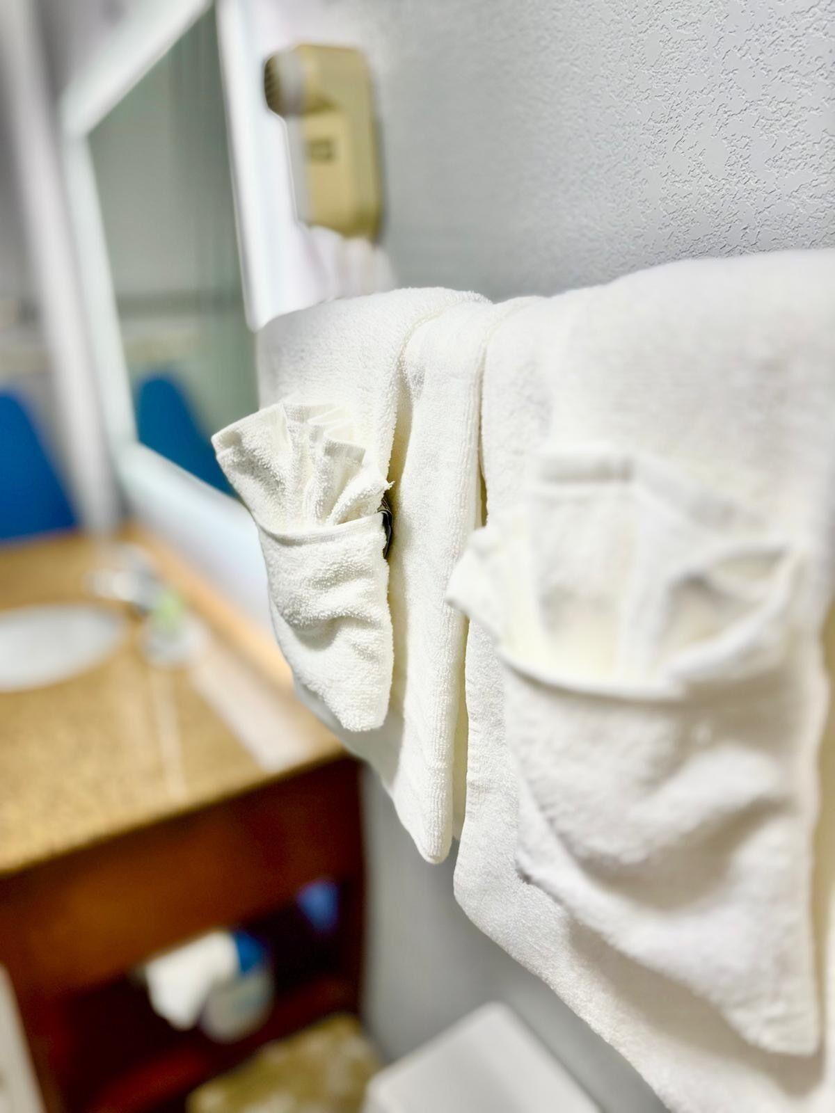 Une serviette blanche est accrochée au mur d’une salle de bain, avec un comptoir en bois et un miroir en arrière-plan.