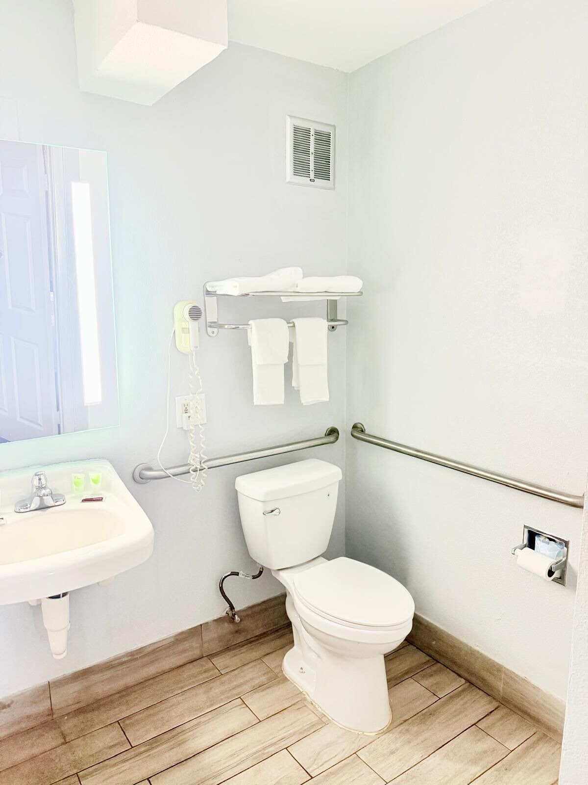 A bathroom with a toilet, sink, towel rack, and handrails.