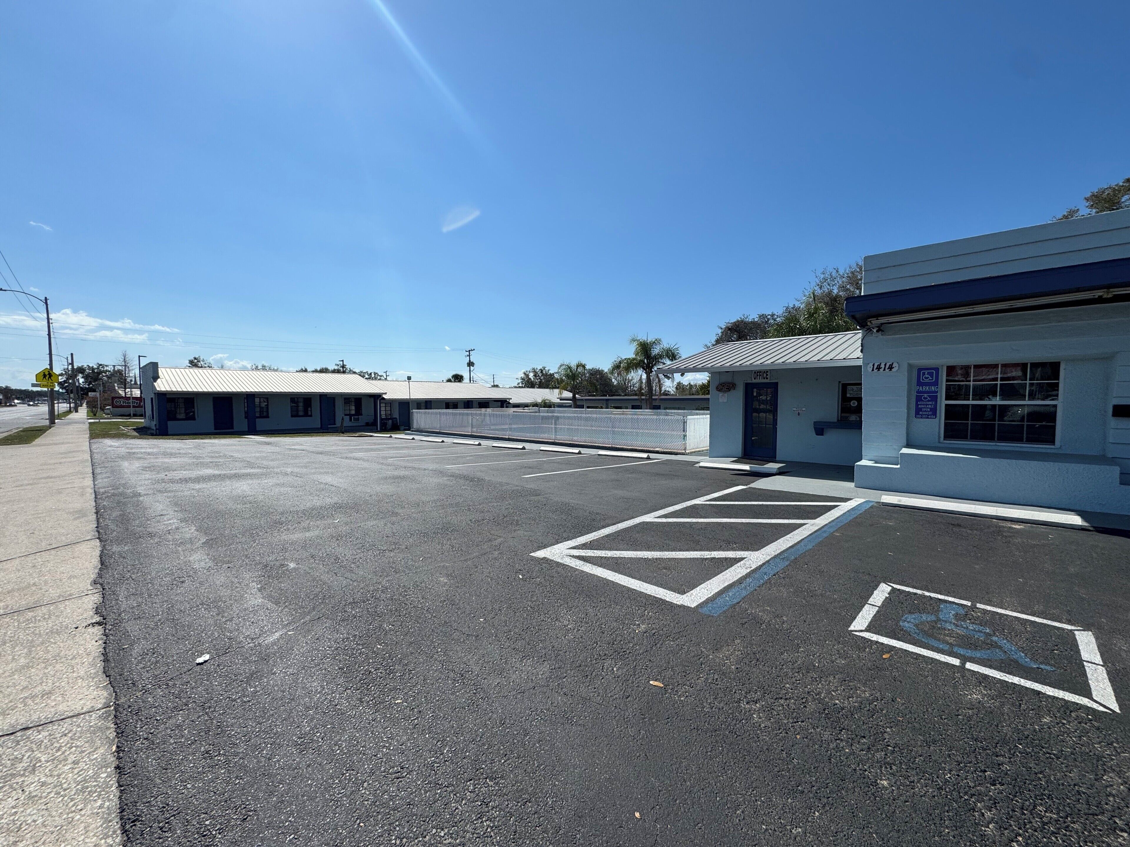 Un parking avec des places réservées aux personnes handicapées, un bâtiment portant l’inscription « Bureau », et un ciel bleu dégagé.