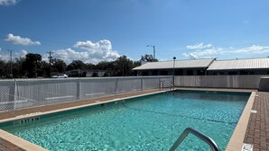 Une piscine à l’eau claire, entourée d’une terrasse en briques et de rampes en métal.