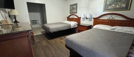 A hotel room with two beds, a desk, a lamp, and a painting on the wall.