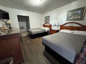 A hotel room with two beds, a desk, a lamp, and a painting on the wall.