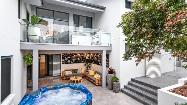 A modern outdoor living area with a hot tub, seating, and a tree.