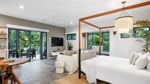 A modern bedroom with a large bed, a dining area with a table and chairs, and a TV mounted on the wall.