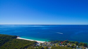 An aerial view of a coastal area with a beach, clear blue waters, and a small settlement with houses.