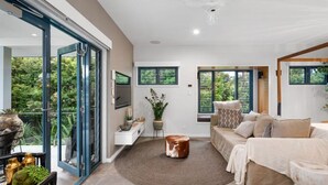 A spacious living room with a large window, a sofa, a coffee table, and a TV mounted on the wall.