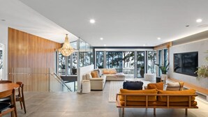 A modern living room with a sofa, a dining table, and a staircase leading to an upper level. - 5 BDR - 250m to Beach - Outdoor Spa - Book 3 Nights, Pay for 2 until 24 September 2026 (Hyams Beach)