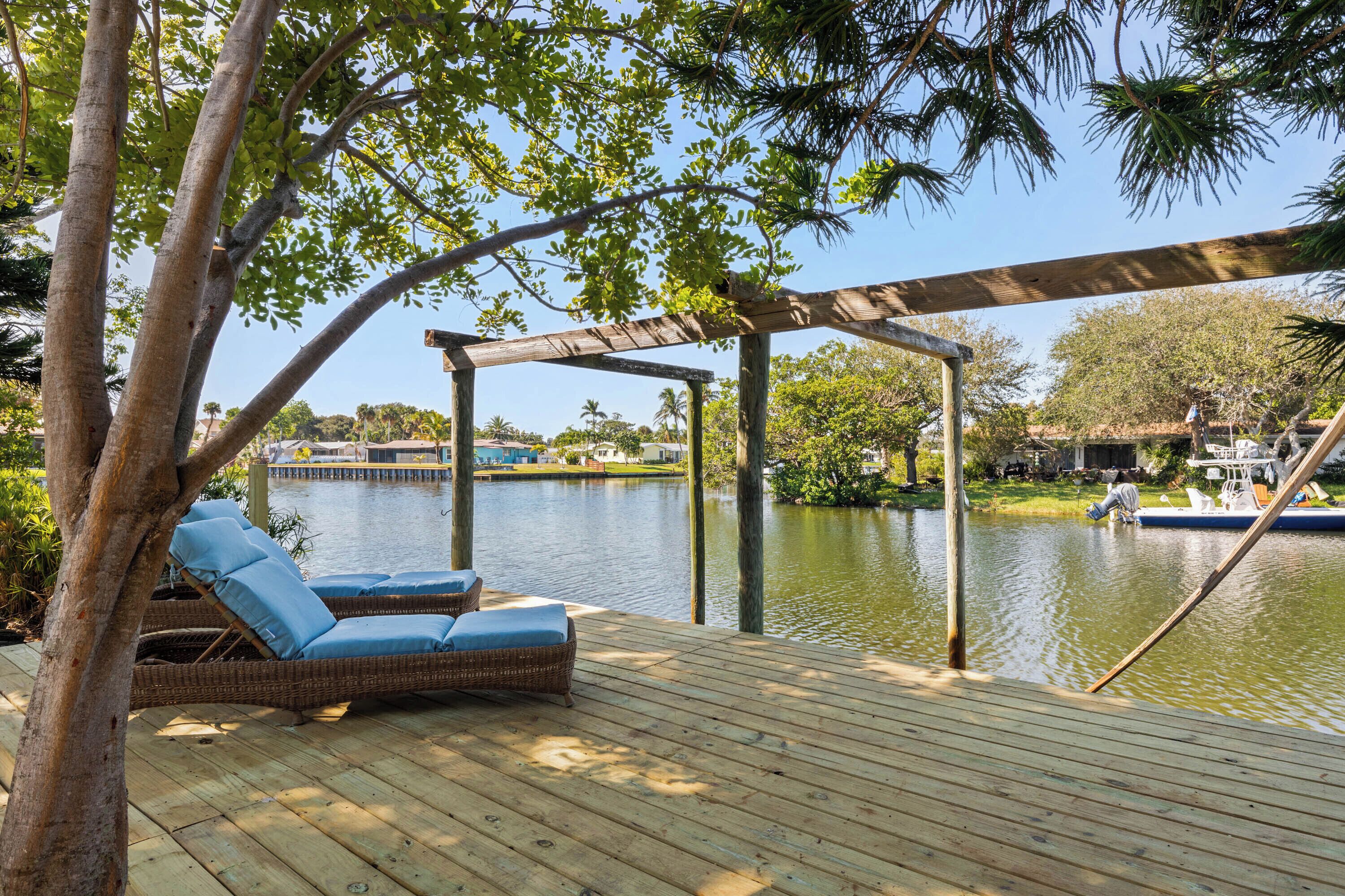 Una terraza de madera con sillones de mimbre y una pérgola con vista a una masa de agua tranquila.