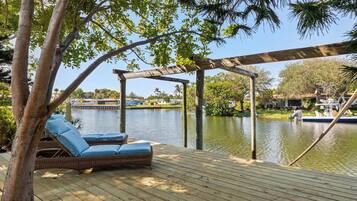 Una terraza de madera con sillones de mimbre y una pérgola con vista a una masa de agua tranquila.