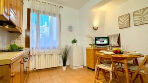 A kitchen with wooden cabinets, a stove, a sink, a dining table with chairs, a TV, and a potted plant. - Ca' de le Chiovere (Cannaregio) (Venecia)