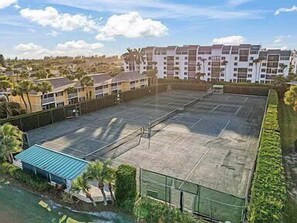 Uma quadra de tênis cercada por uma grade, com um edifício ao fundo.