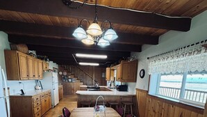 A kitchen with wooden cabinets, a central island with a fruit basket, and a view through the window. - Welcome to Crane Meadows, West Yellowstone Cabin, sleeps 32 close to Hebgen Lake (West Yellowstone)