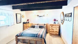 A bedroom with a wooden bed, a nightstand, a dresser, and a mirror. There is a window with curtains and a wall-mounted light fixture. - Welcome to Crane Meadows, West Yellowstone Cabin, sleeps 32 close to Hebgen Lake (West Yellowstone)