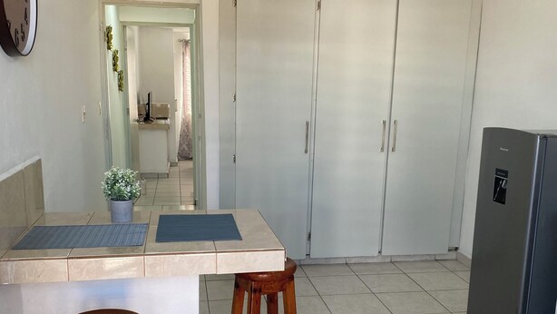A kitchen with a countertop, two stools, a refrigerator, and a door leading to another room.