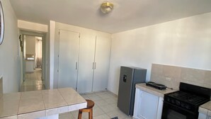 A kitchen with a white countertop, two wooden stools, a black stove, a refrigerator, and a tiled floor.