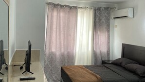 A bedroom with a bed, a desk with a computer, a chair, and a window with curtains.