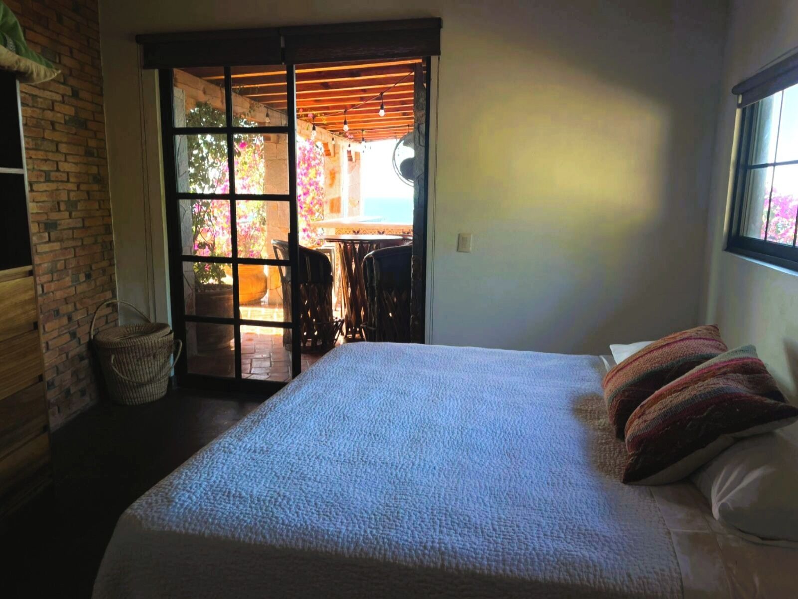 A bedroom with a large bed, a wooden door leading to an outdoor area with a table and chairs, and a window with a view.