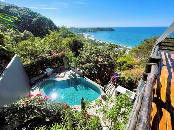 Ein Pool, umgeben von üppiger Vegetation und Blick aufs Meer.