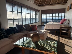 Ein geräumiges Zimmer mit großem Fenster und schöner Aussicht, einem Glastisch mit dekorativer Vase und einem gemütlichen Bett mit Kissen.