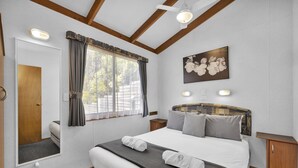A bedroom with a large bed, a wooden headboard, a window with curtains, a painting on the wall, and a bedside table. - 2 Bedroom Superior Villa (Metung)