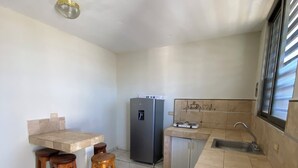 Cocina compacta con refrigerador, pileta, una pequeña barra y dos taburetes de madera.