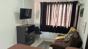 Una habitación con cama, televisor, escritorio y ventana con cortinas.