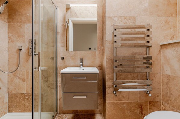 A modern bathroom with a glass shower enclosure, a sink with a mirror above it, and a towel rack with multiple towels.