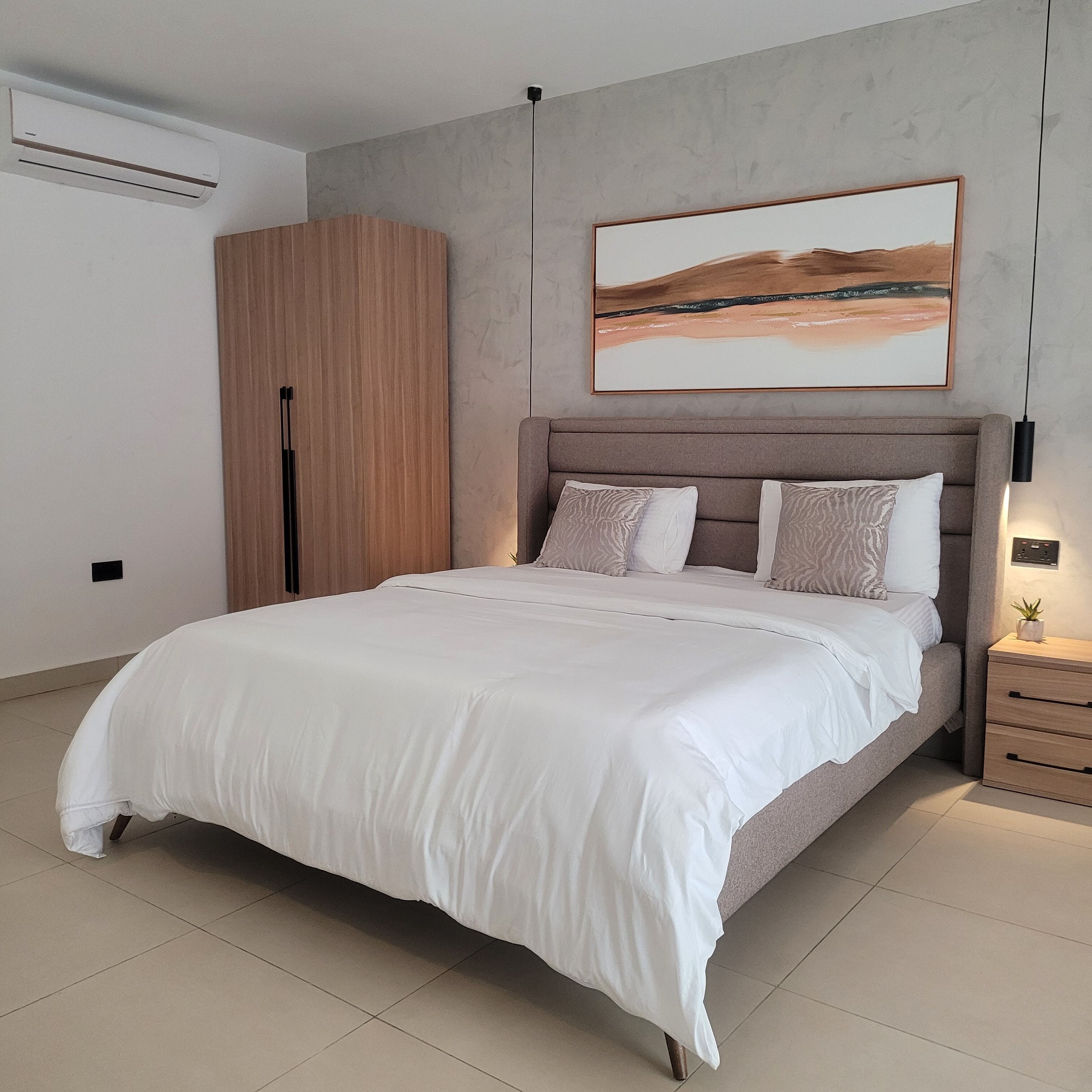 A modern bedroom with a large bed, a wardrobe, a nightstand, and a painting on the wall.