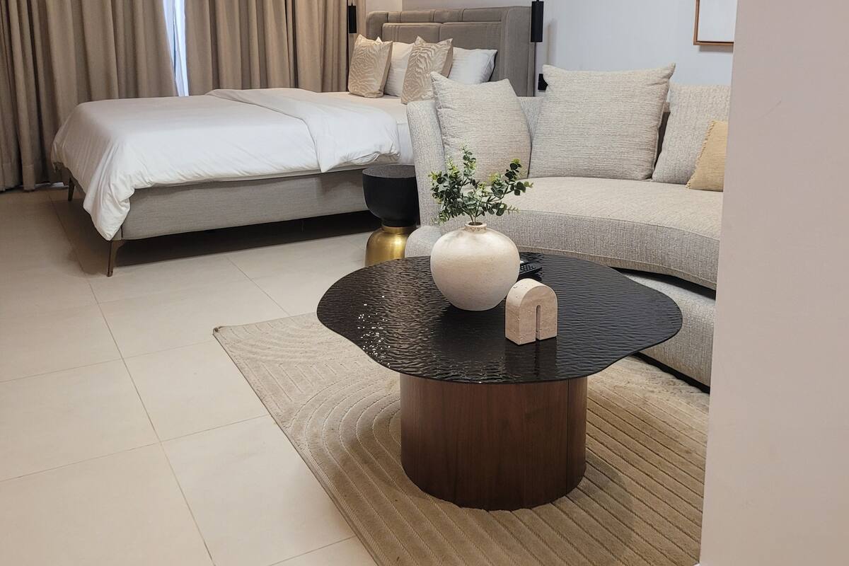 A modern bedroom with a bed, a sofa, a coffee table with decorative items, and a painting on the wall.