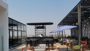 A rooftop bar with outdoor seating, a bar counter, and a view of the city. - RT properties at Belrose Place (Accra)