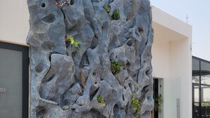 A modern building with a textured rock facade, a glass door, and a small planter with plants. - RT properties at Belrose Place (Accra)