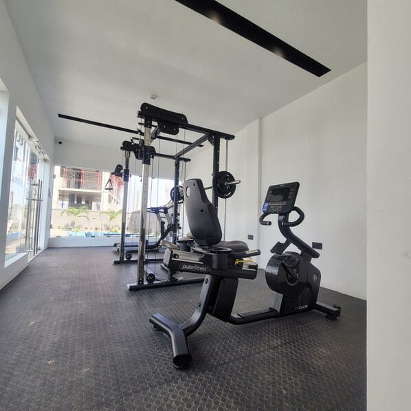 A gym with cardio machines, weightlifting equipment, and a large window providing a view of the outside.