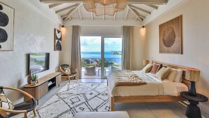 Quarto com cama, televisão, sofá e vista para o oceano.