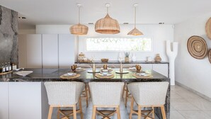 Uma cozinha moderna com uma ilha central, três luminárias pendentes de vime e uma janela ampla.