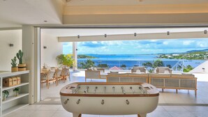 Um quarto amplo com mesa de pebolim, área de jantar com vista para o oceano e varanda com mobiliário para área externa.