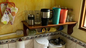 Uma cozinha com cafeteira, cozido de arroz e diversos utensílios de cozinha em uma estante de madeira.