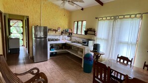 Uma cozinha com área de refeições, cadeiras de madeira, um ventilador de teto e uma geladeira.