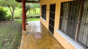 Uma galeria coberta com piso de concreto, vigas de madeira e uma parede amarela.