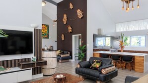 Una sala de estar moderna con un televisor de pantalla plana grande, un sofá de cuero negro, una mesa de centro de madera y una zona de comedor con barra.