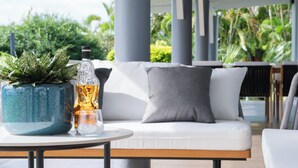 Un área de estar exterior moderna con un sofá blanco, una mesa redonda, una planta en maceta y una botella de licor.