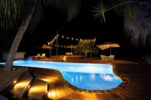 A nighttime outdoor swimming pool area with a wooden deck, lounge chairs, and string lights. - Fiji's Best Family Vacation Home . Spectacular Ocean Views w/Chef's Kitchen ! (Western Division)